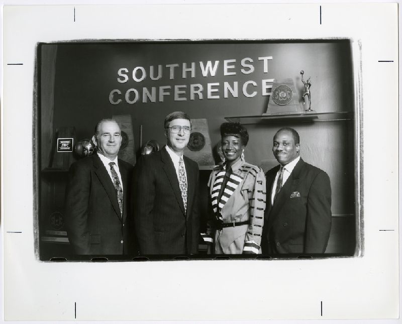 Group posing in front of the Southwest Conference wall of trophies