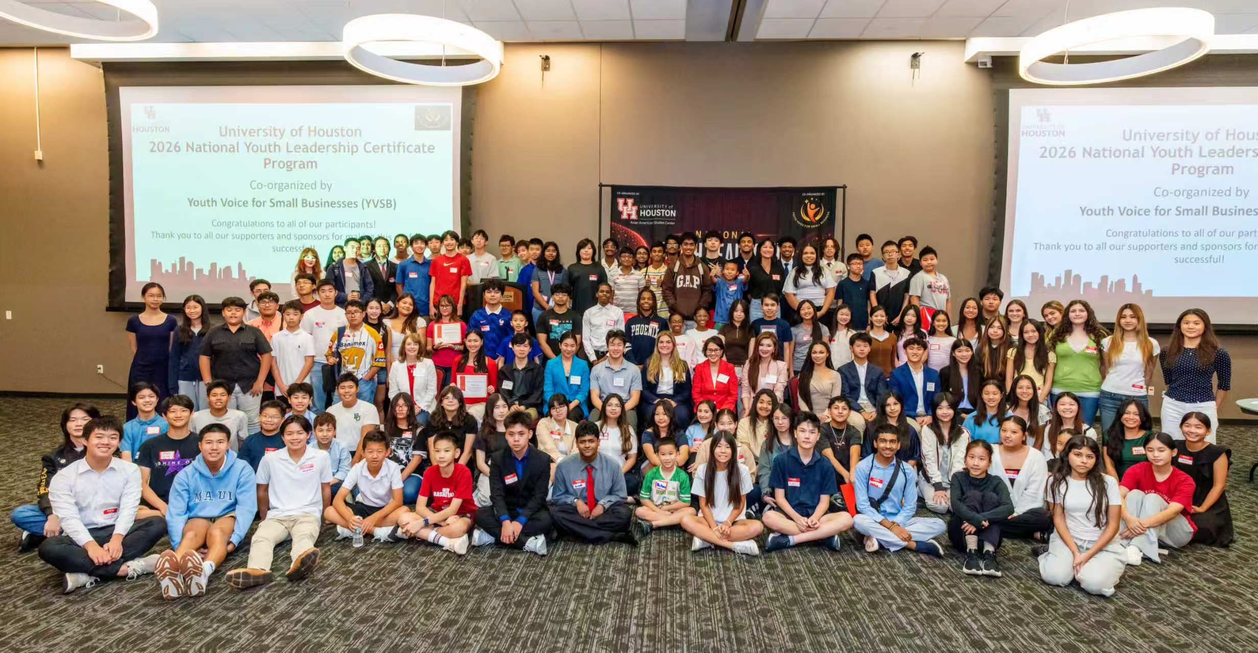 140 conference attendees and panelists pose for a large group photo in the conference ballroom.