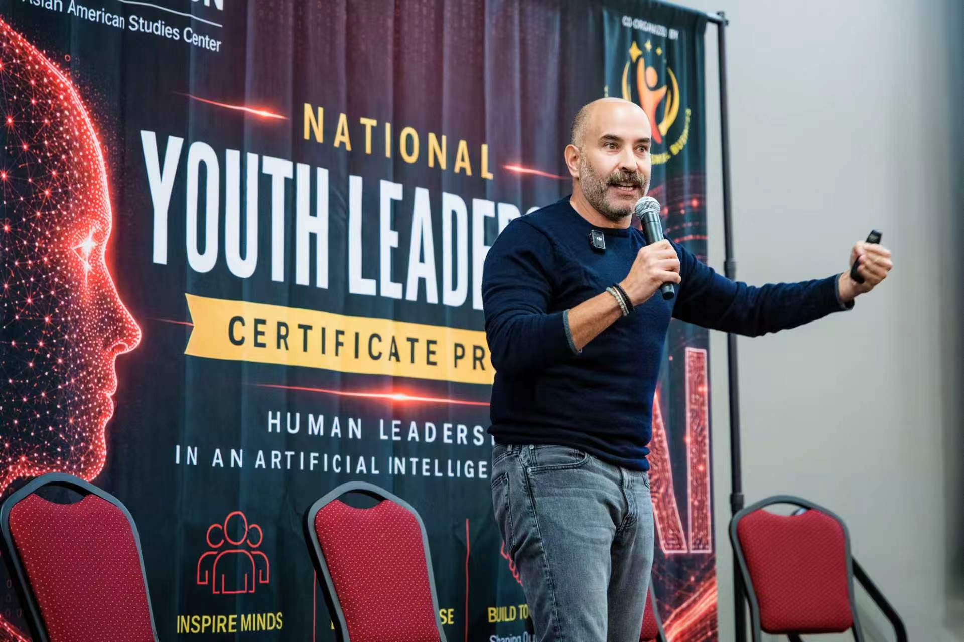 Keynote speaker Mark Dibella speaks on stage with a conference banner featuring a futuristic face behind him.