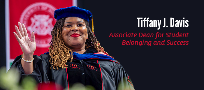 A black woman with graduation regalia smiling with her hand raised; Associate Dean for Student Belonging and Success, Tiffany J. Davis