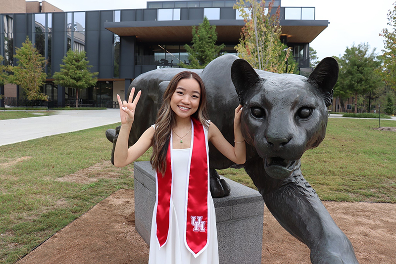 Woman with regalia sitting in front of a cougar statue