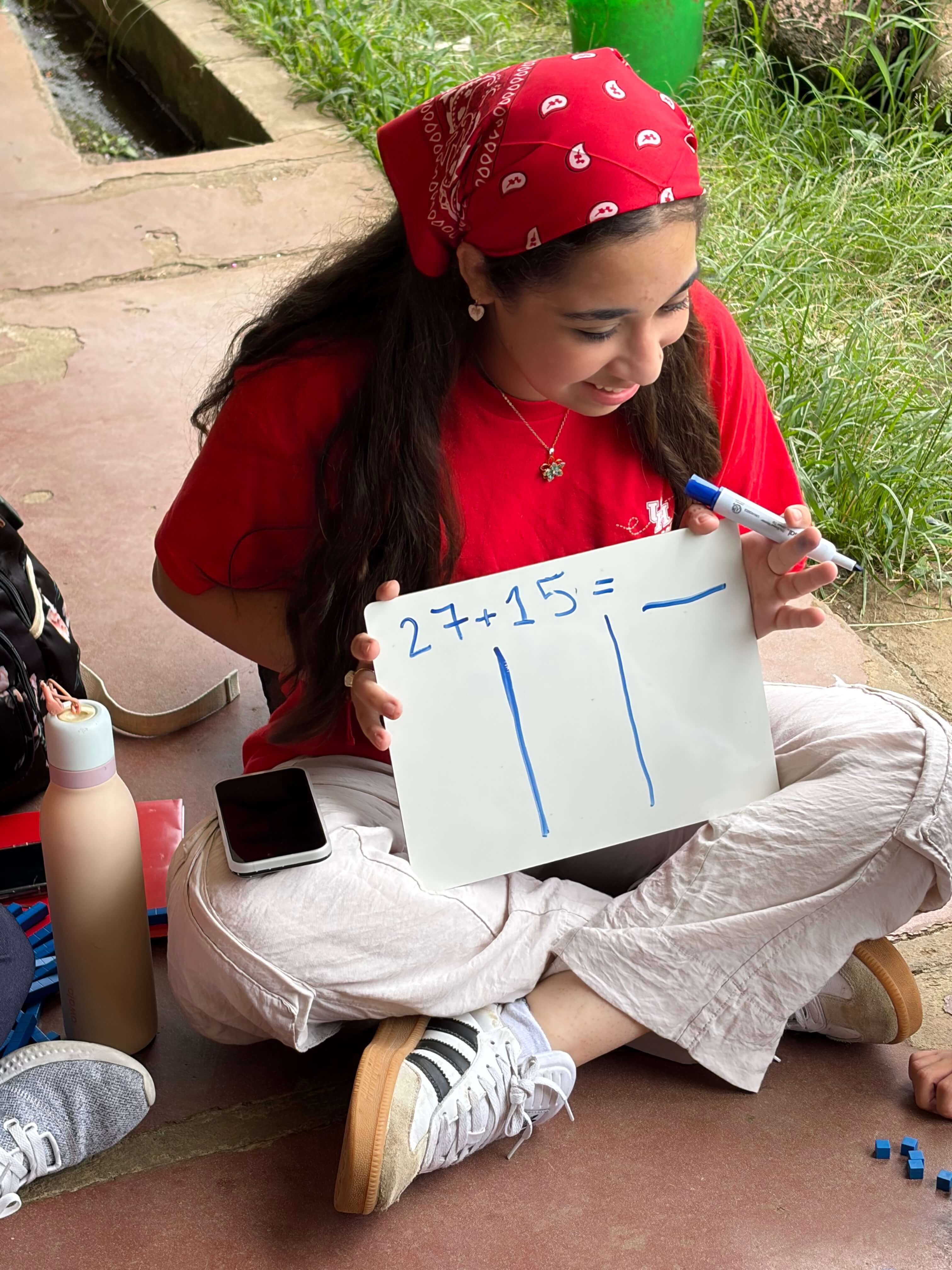 Areeba Sohail holds a whiteboard with a math problem in her lap sitting outside