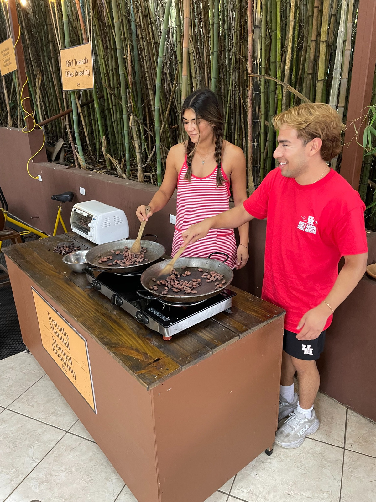 Two students cook meat on an outdoor skillet.