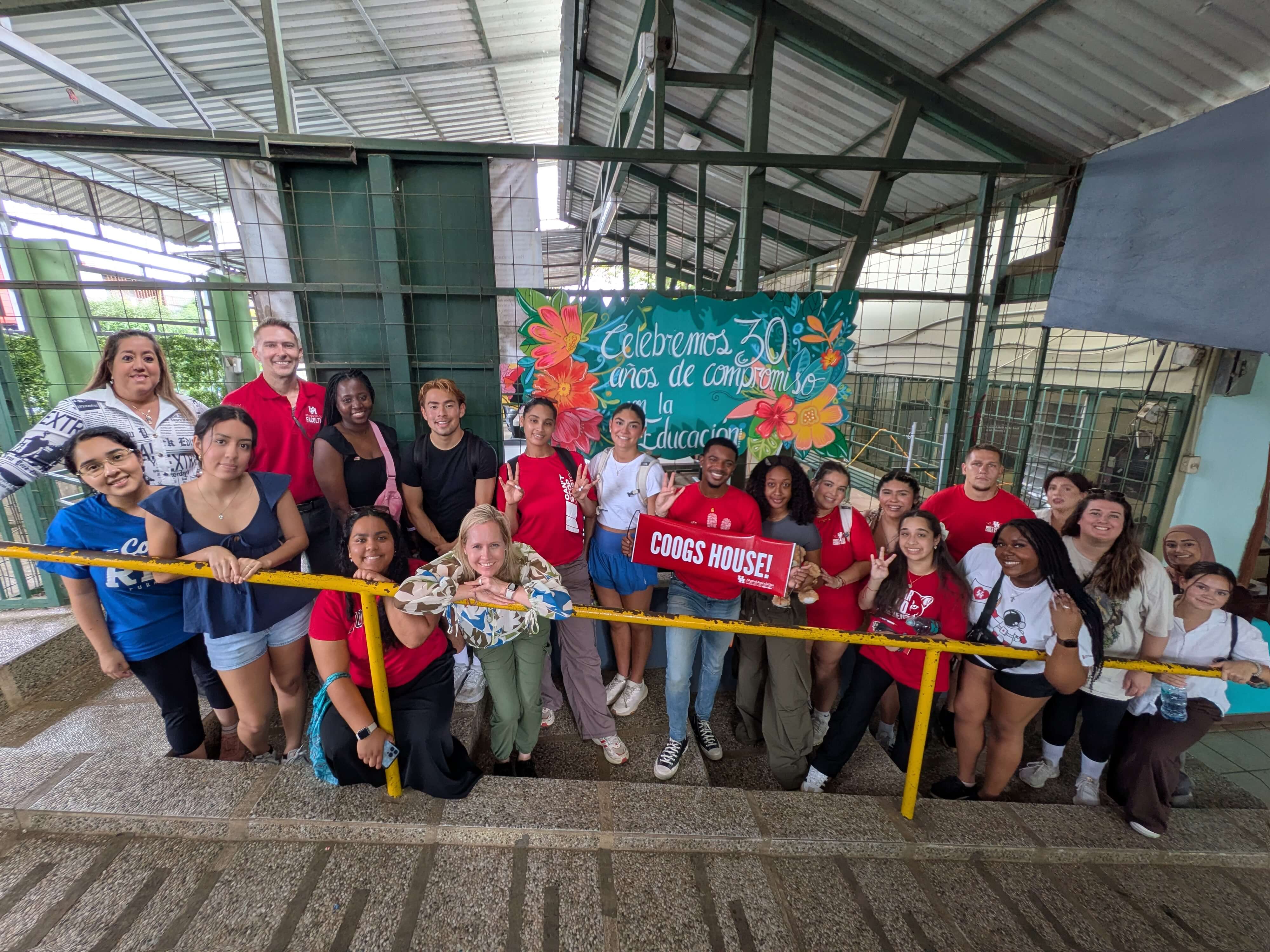 Students and faculty on the learning abroad trip post together holding a sign that says Coogs House with a Spanish sign behind them.