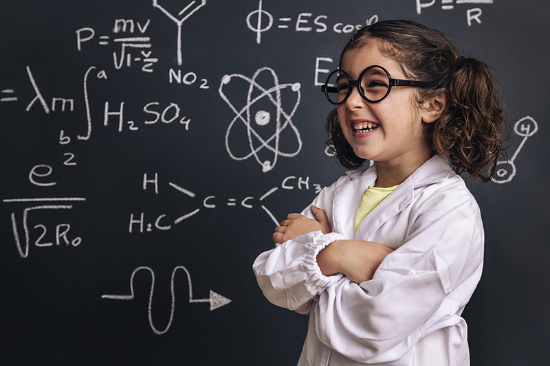 Young girl in a white coat in front of a blackboard