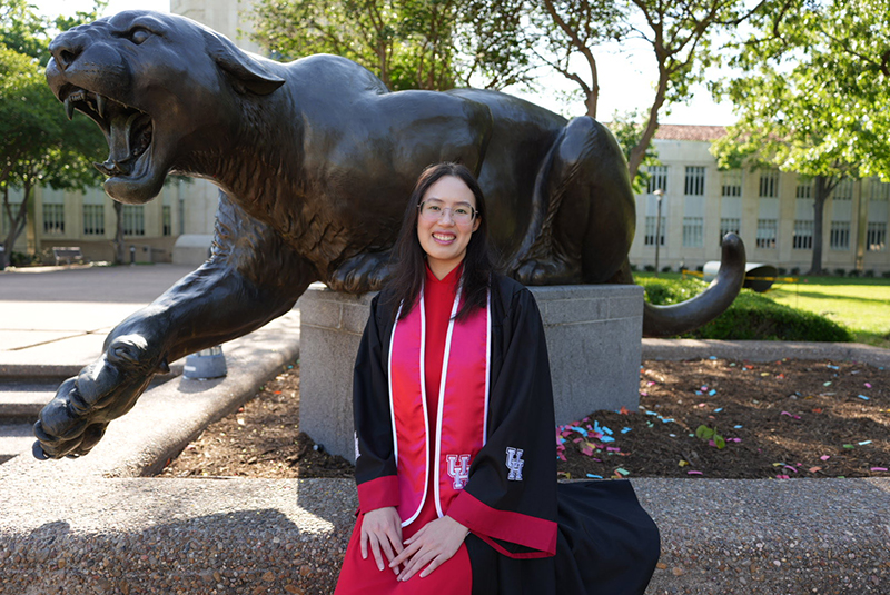 Student in regalia sitting in front of the Cougar statue