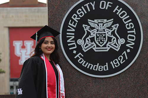 Woman with black hair wearing regalia in front of a sign that says "University of Houston; Founded 1927
