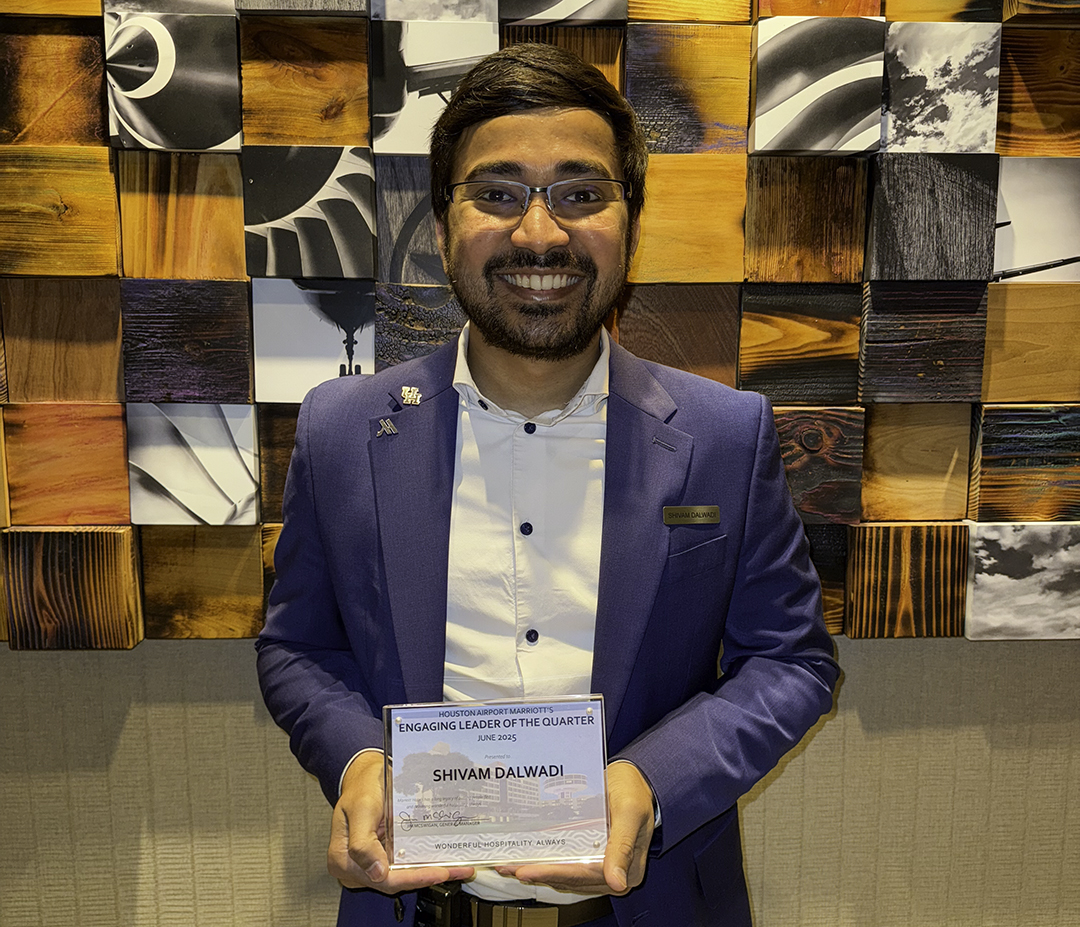 Shivam Dalwadi holding an award in front of wood art intalation at his workplace