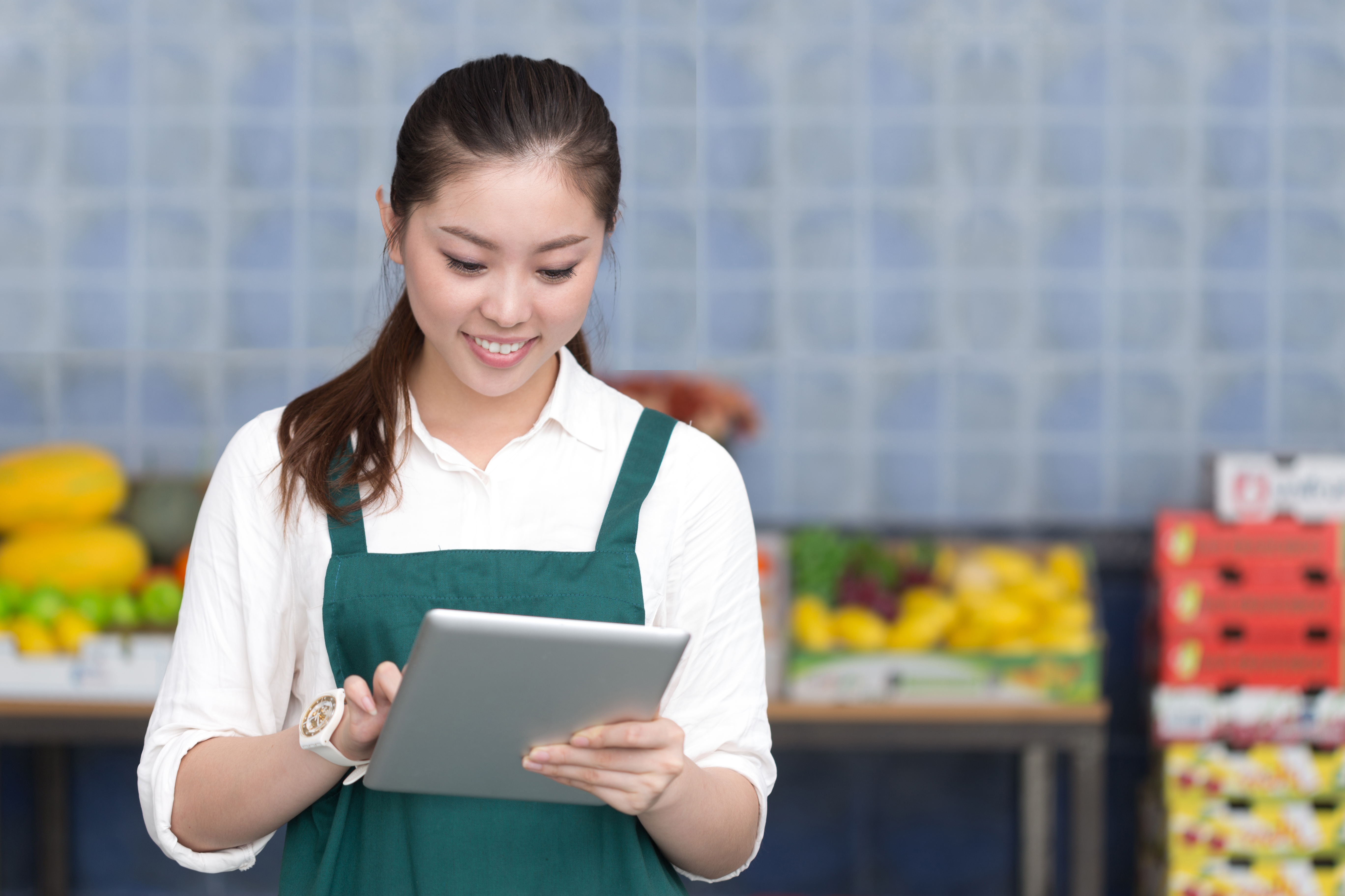 Smiling grocery worker using a tablet in front of fresh produce.