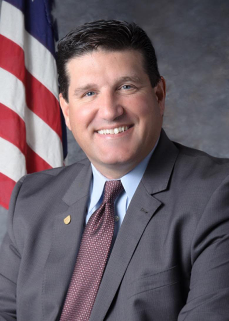 white male in business suit with an american flag background