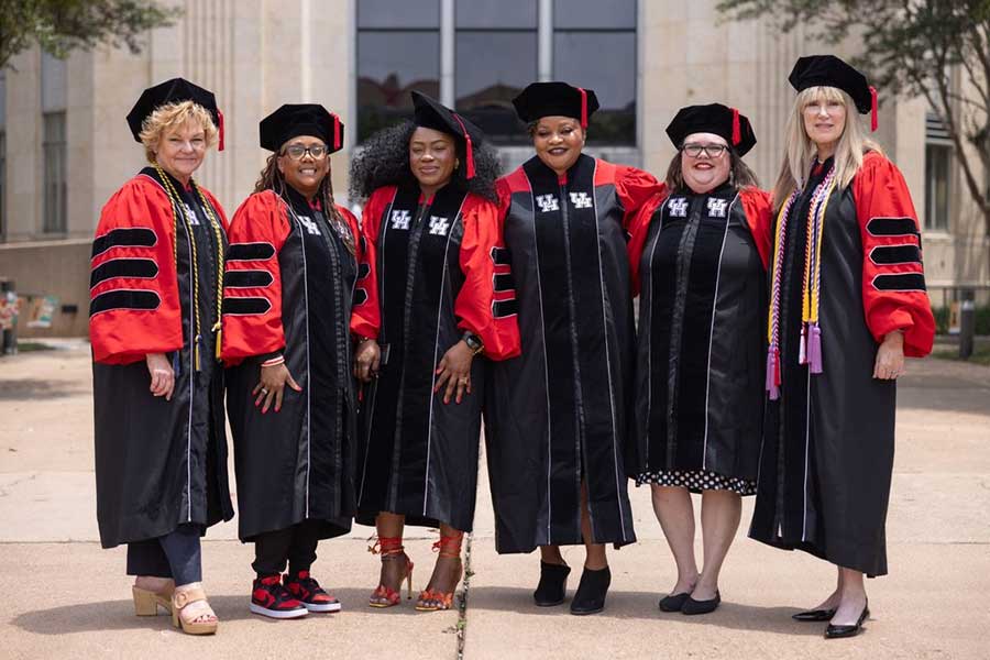 A group of women in black and red graduation regalia stand together.