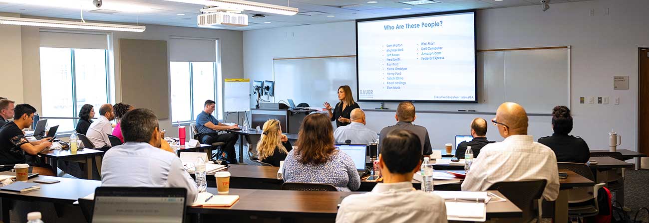A group od professions sit in a lecture room as an instructor presents.