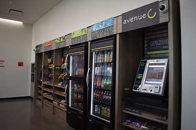 Convenience store shelving along a wall stocked with various snacks and drinks. A check out kiosk is at the far right.