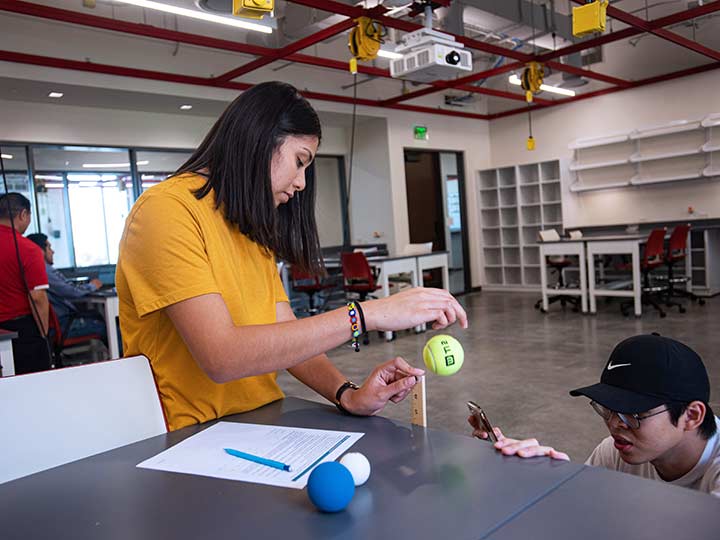 Groups of students work together at tables.