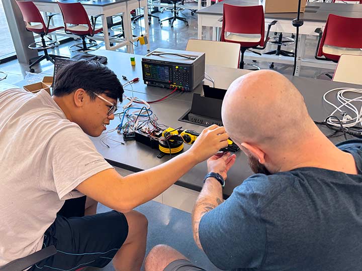 Two students work on a small mechanical arm together.