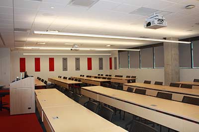 A large classroom with two sets of long rows of desks. A podium is at the front.