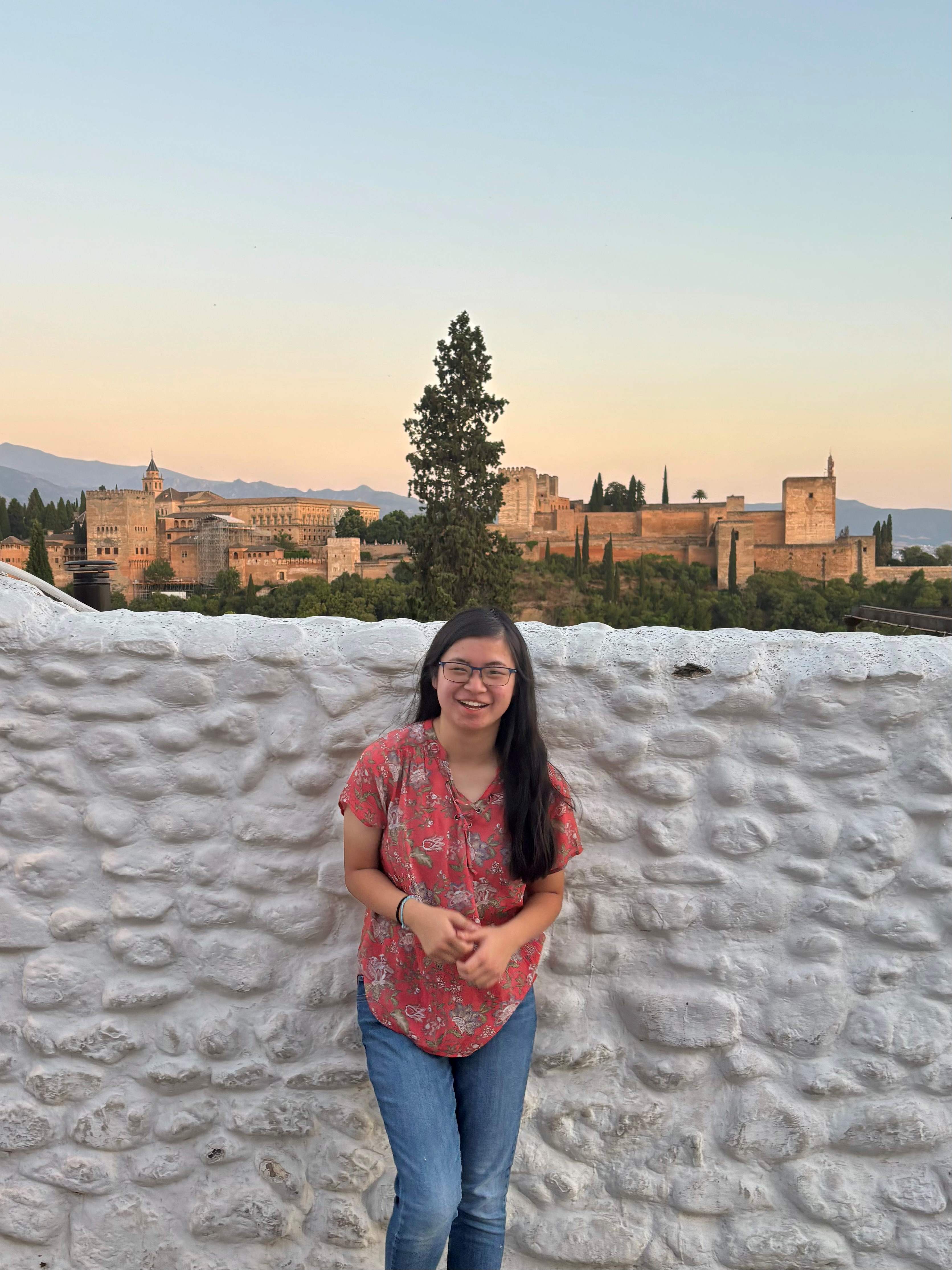 Kayleigh standing in front of a white wall, overlooking an ancient city. 