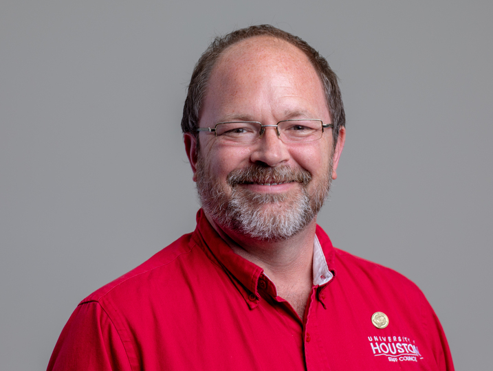 Headshot of Andy Moon wearing a red shirt and smiling in front of a gray backdrop.