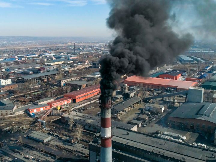 Industrial scene with a factory stack spewing smoke and a train in the background.