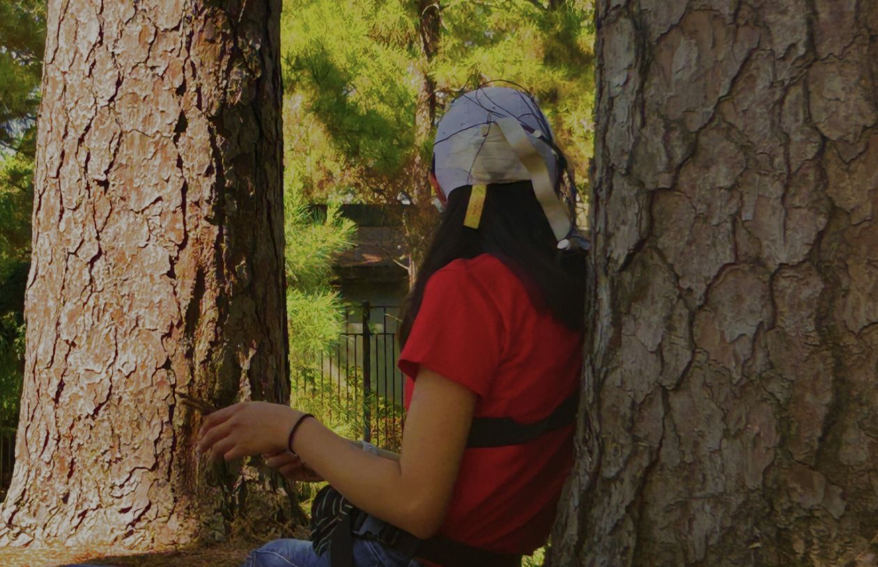 Person wearing brain cap sits between two trees in natural park.