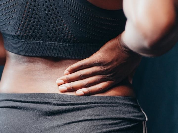 Person holding their lower back, wearing athletic gear.