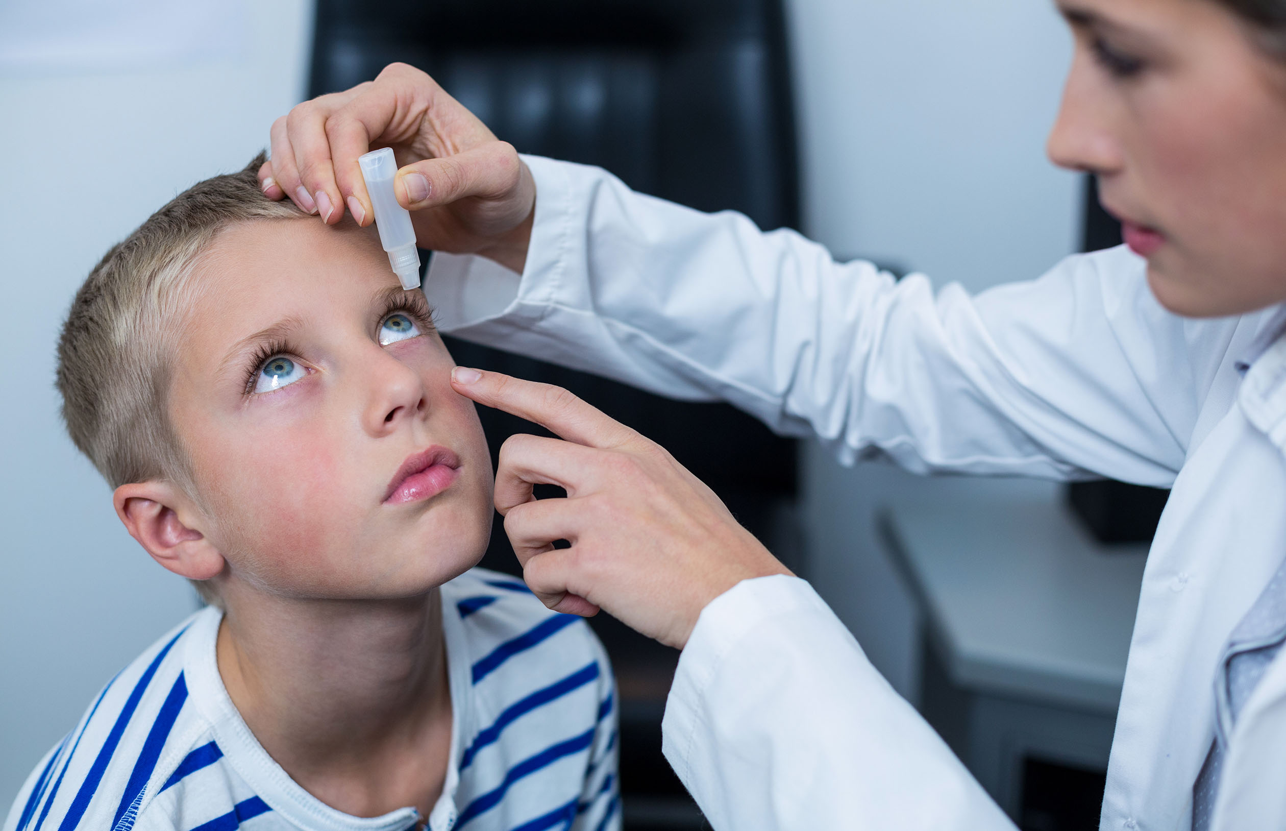 Female optometrist putting eye drop in young patient eyes in ophthalmology clinic