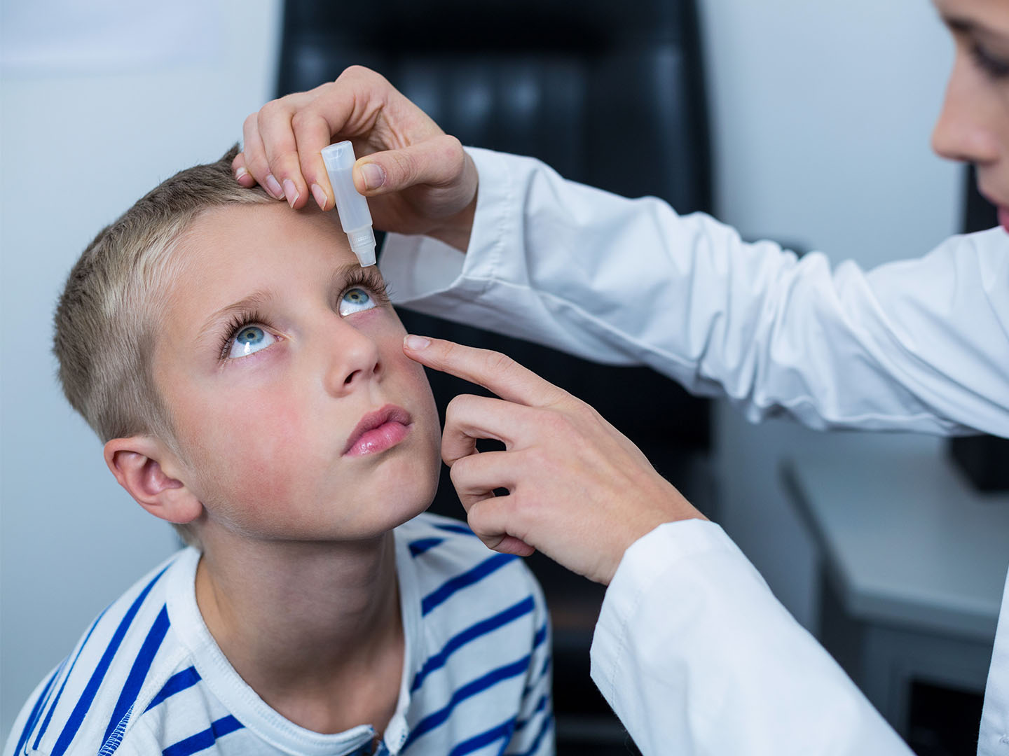 Female optometrist putting eye drop in young patient eyes in ophthalmology clinic