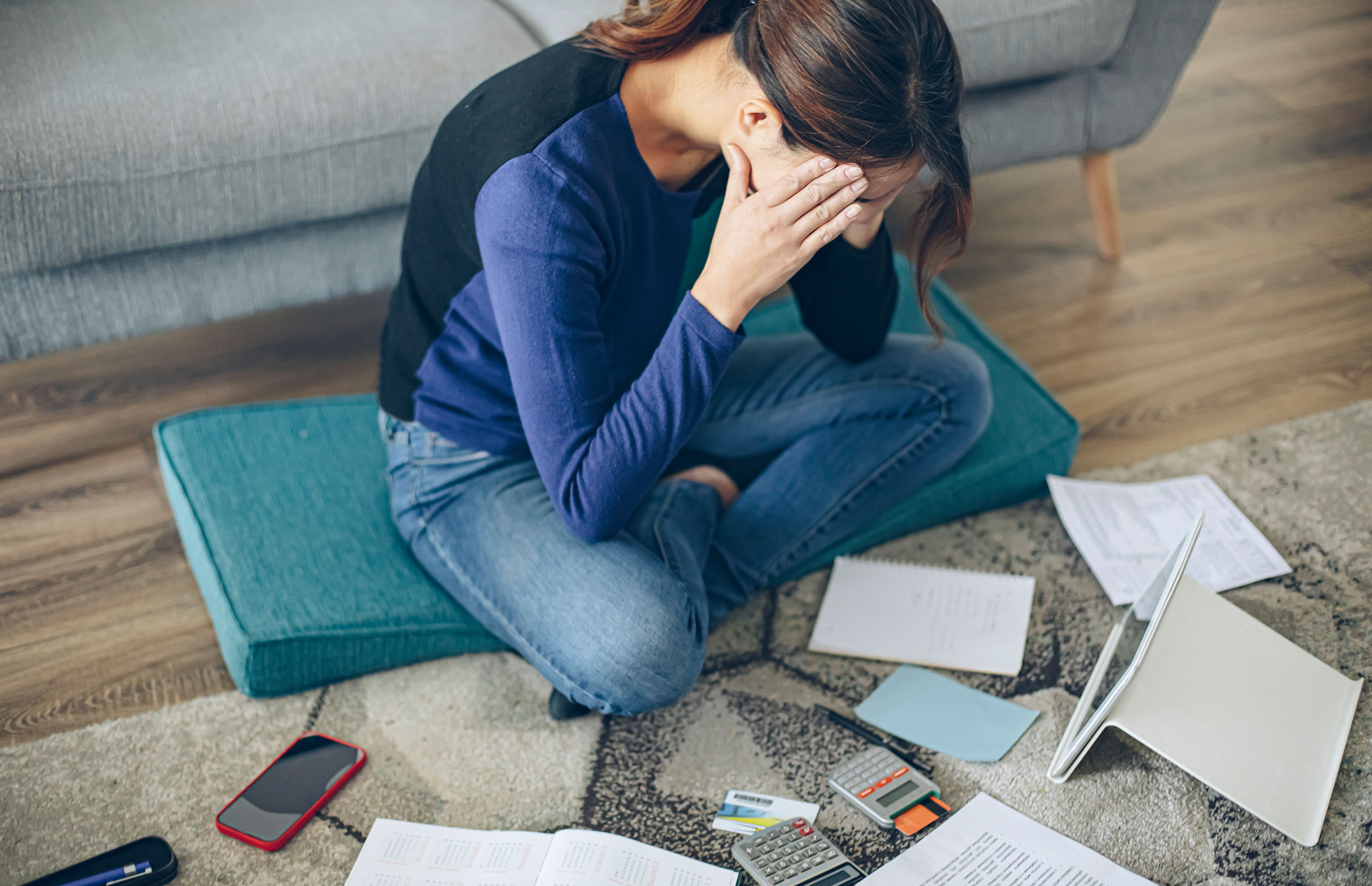 person sitting on floor, looking stressed while surrounded by bills