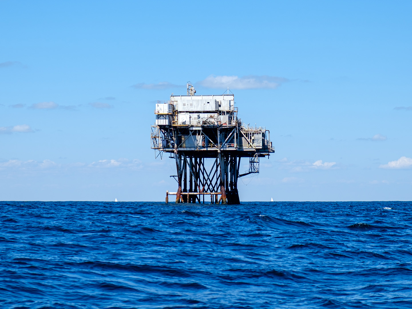 Offshore oil rig with white building and metal legs in blue ocean under blue sky.