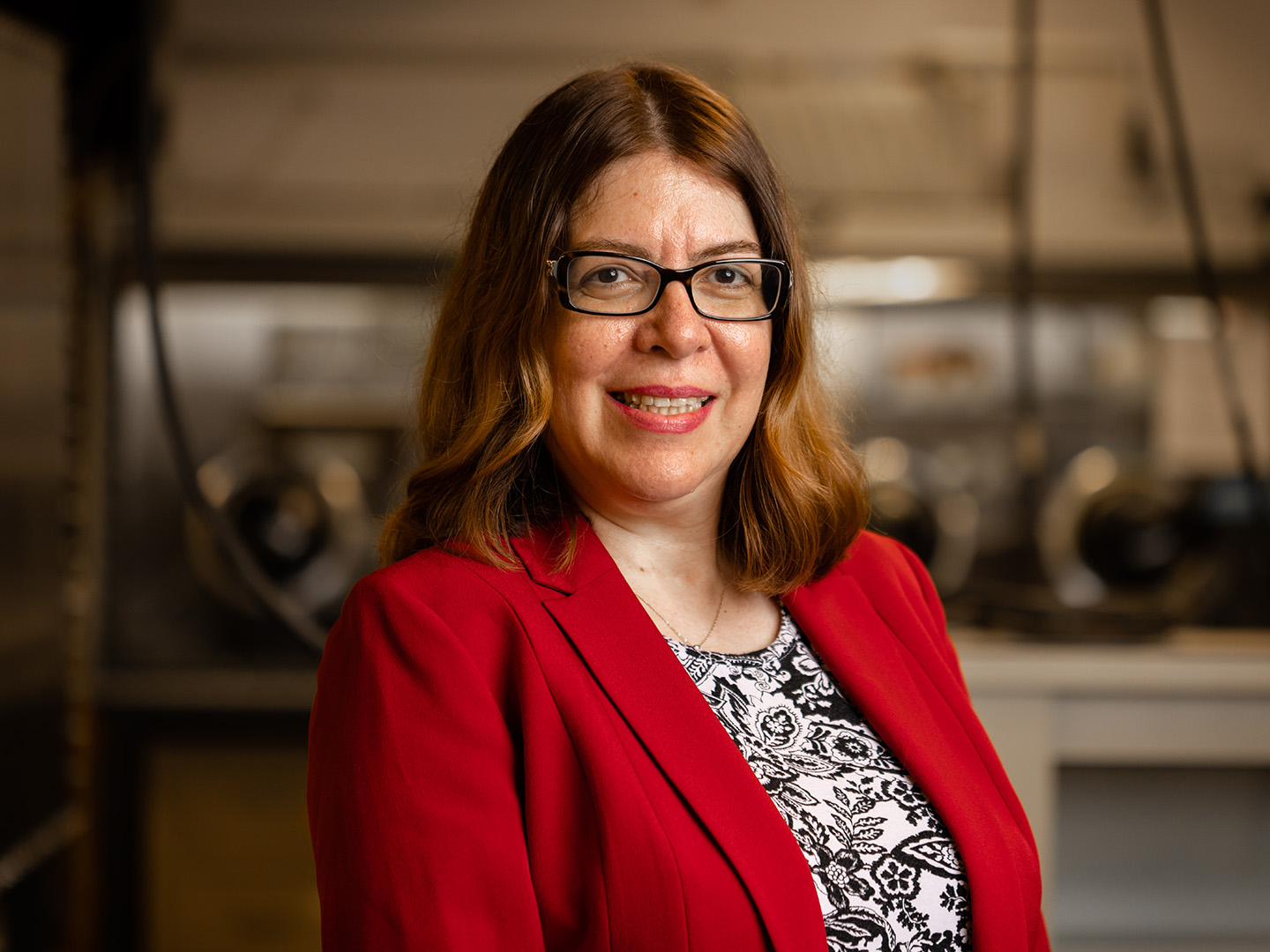 A woman in a red blazer smiling in front of industrial equipment.