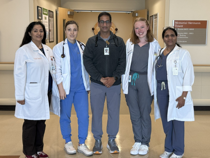 Five medical professionals in scrubs and lab coats posing in a hospital hallway.
