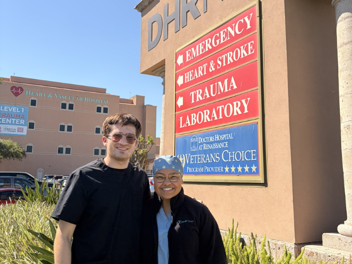 Two people smiling in front of a hospital sign.