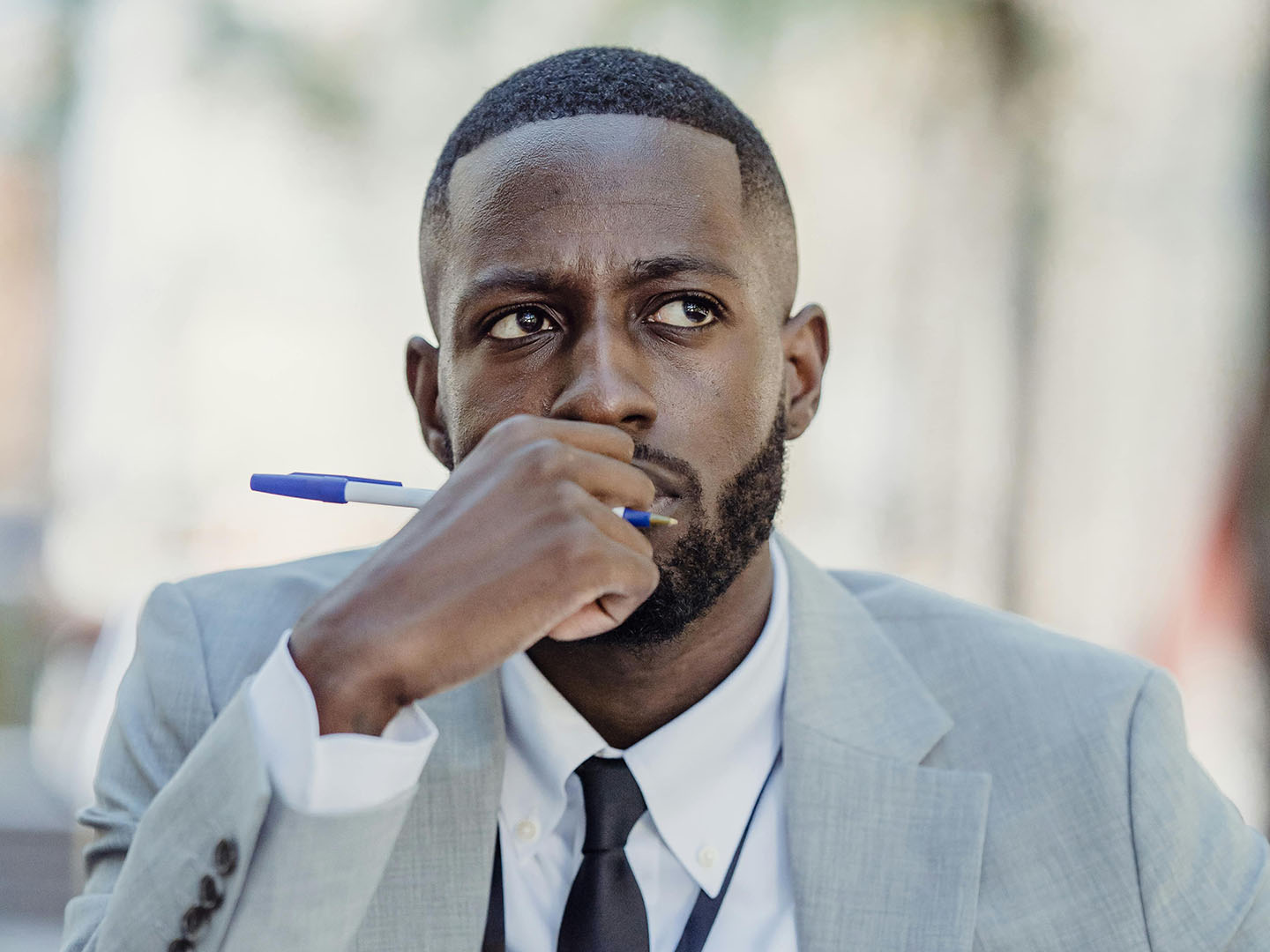 Man in suit holding pen to mouth, looking thoughtful.