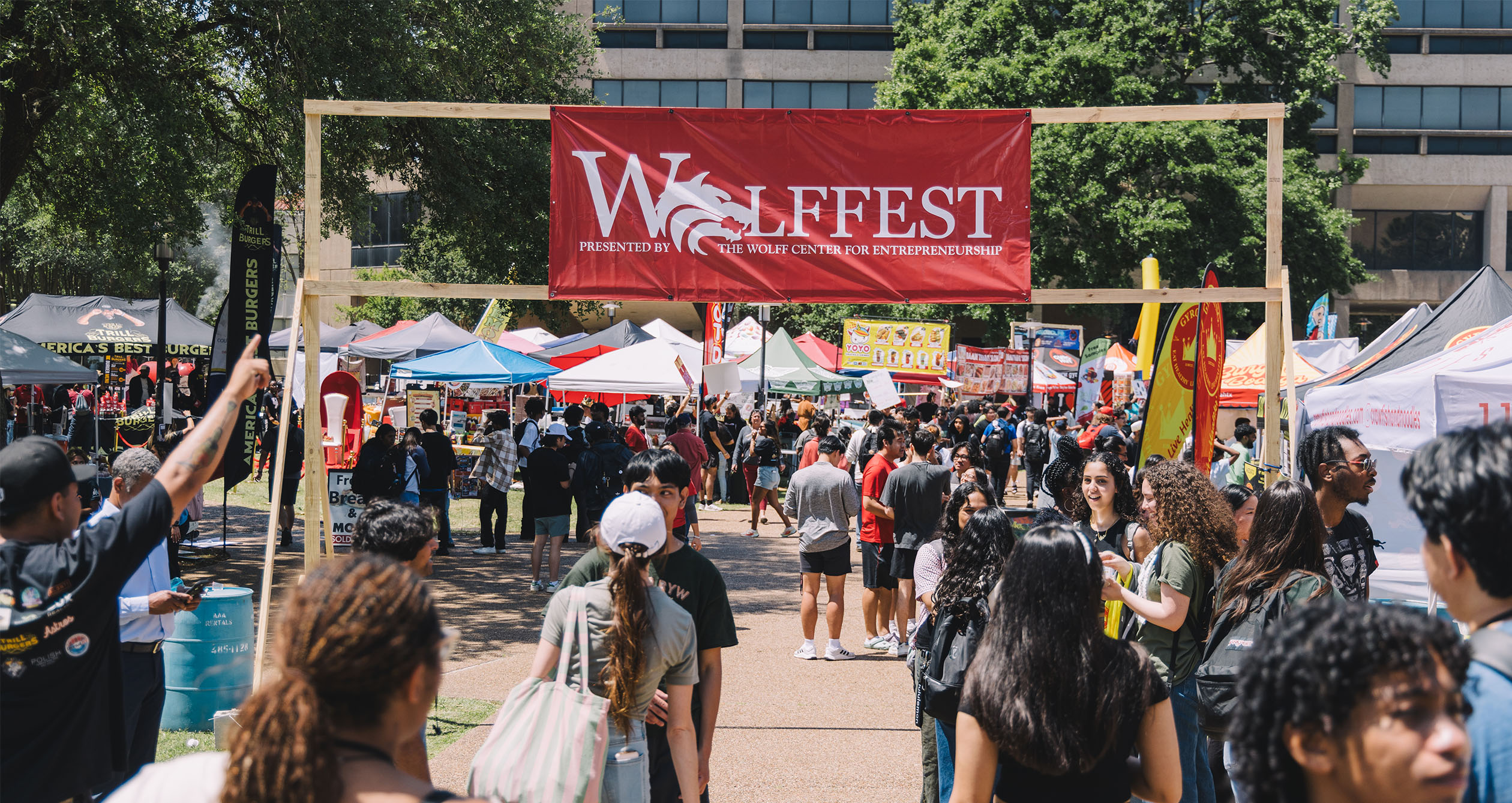 Crowd under red "Wolffest" banner on the UH campus with food stalls.
