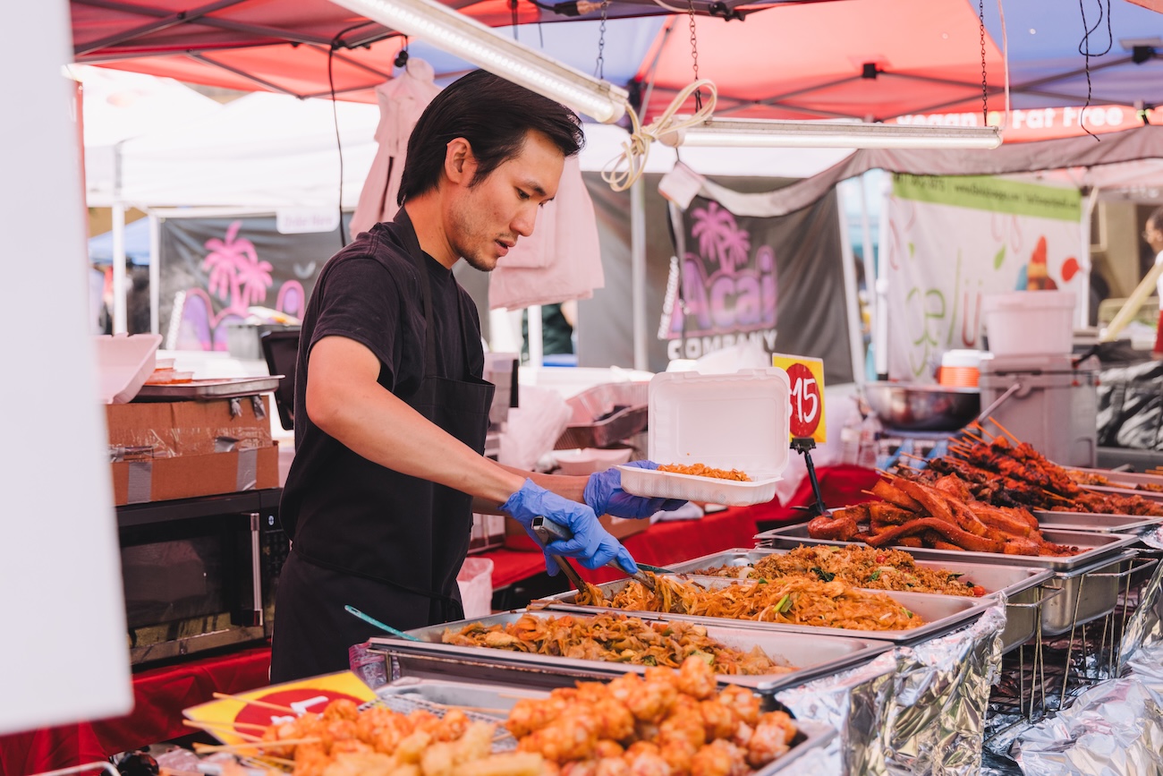 UH student in black shirt and blue gloves serving food from a market stall at Wolffest 2025.