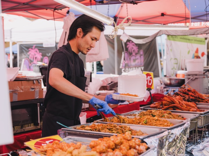 UH student in black shirt and blue gloves serving food from a market stall at Wolffest 2025.