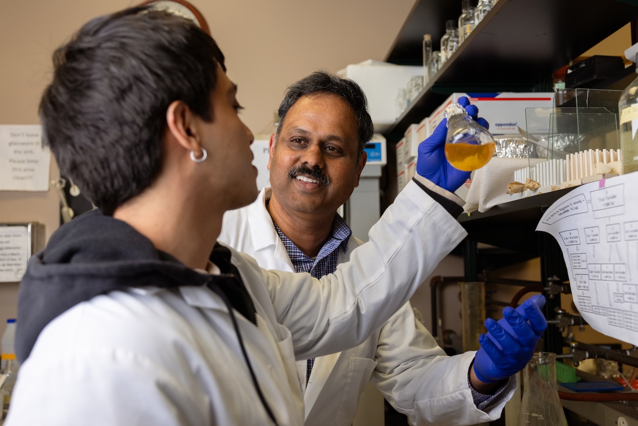 madhan Tirumalai in the lab talking to a student holding a flask with biofilm in it