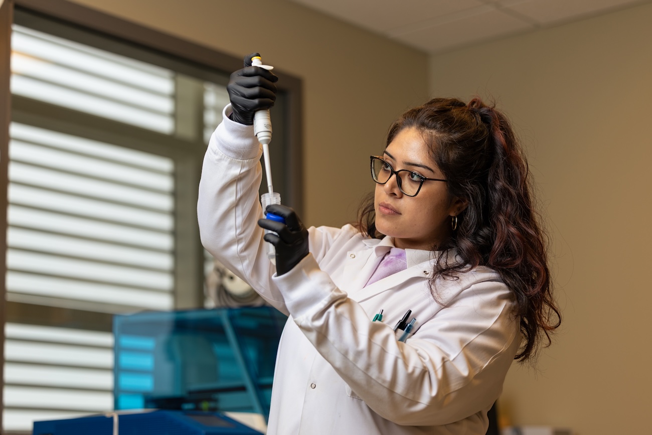 Researcher Ashley Guerrero using a large pipette to place liquid into a large test tube.