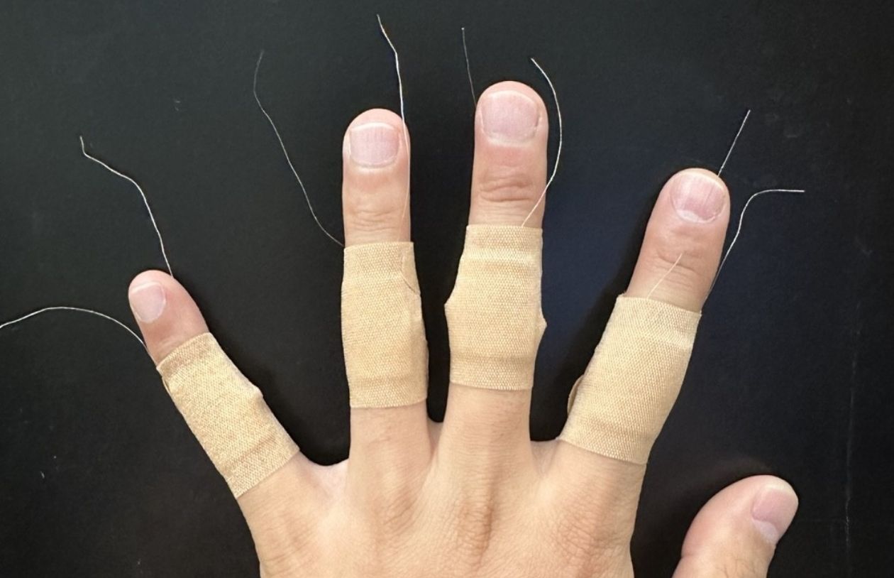 A hand with four fingers wrapped in sensors that look like bandages.