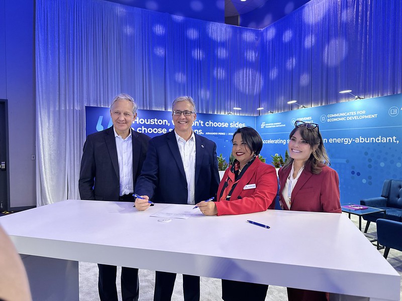 Four people in business attire signing a document at a table with a blue backdrop promoting low-carbon solutions.