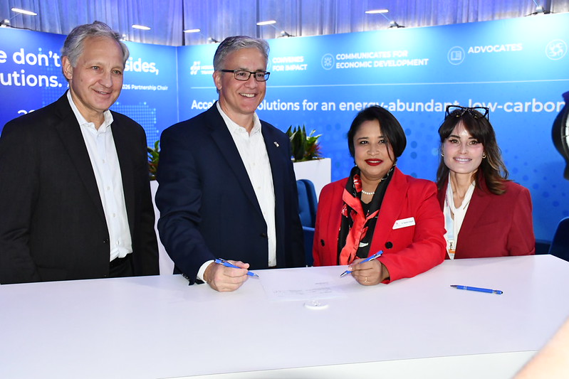 Four people in business attire signing a document at a table with a blue backdrop promoting low-carbon solutions.