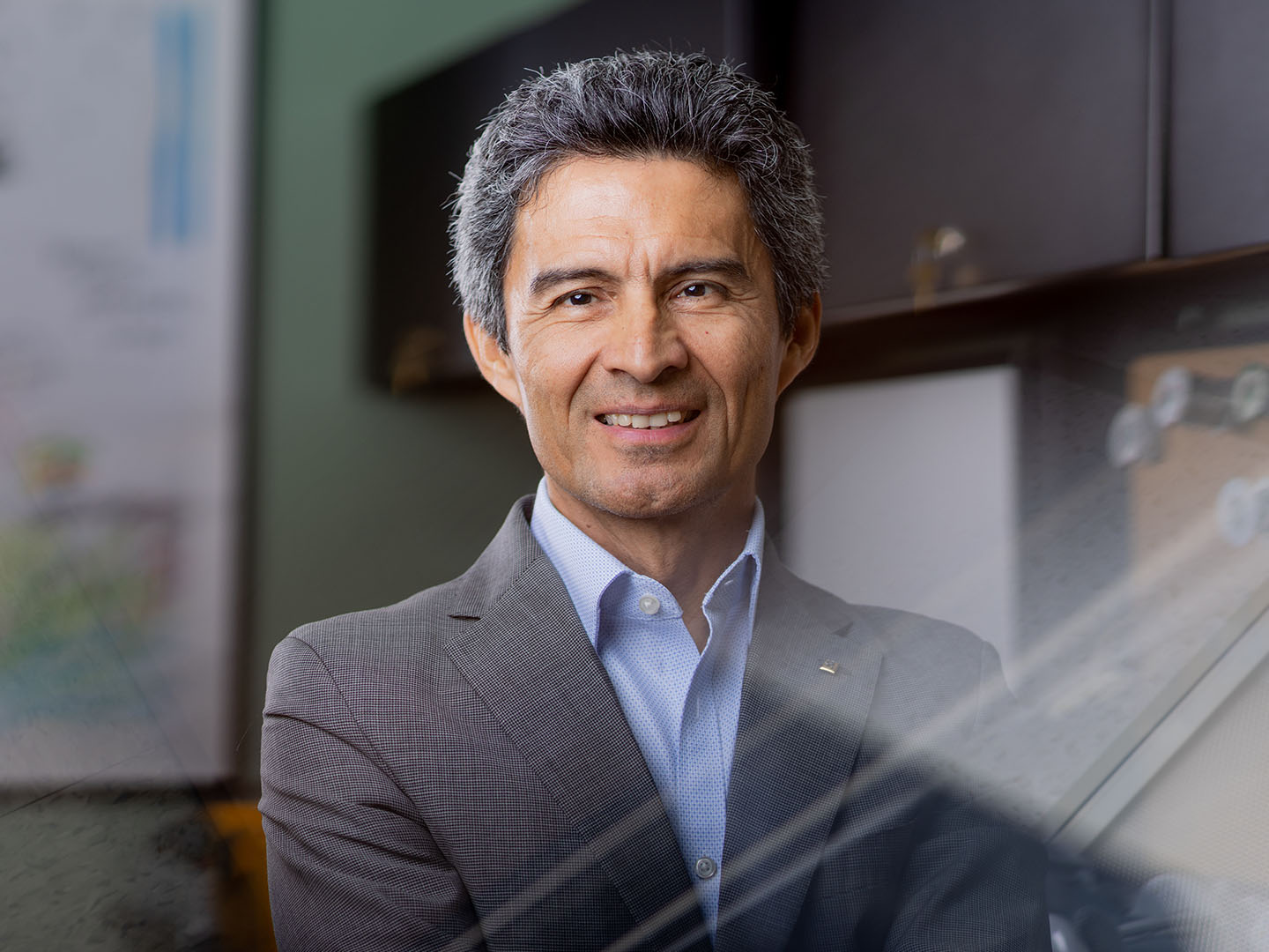 Man in gray suit smiling in front of green wall.
