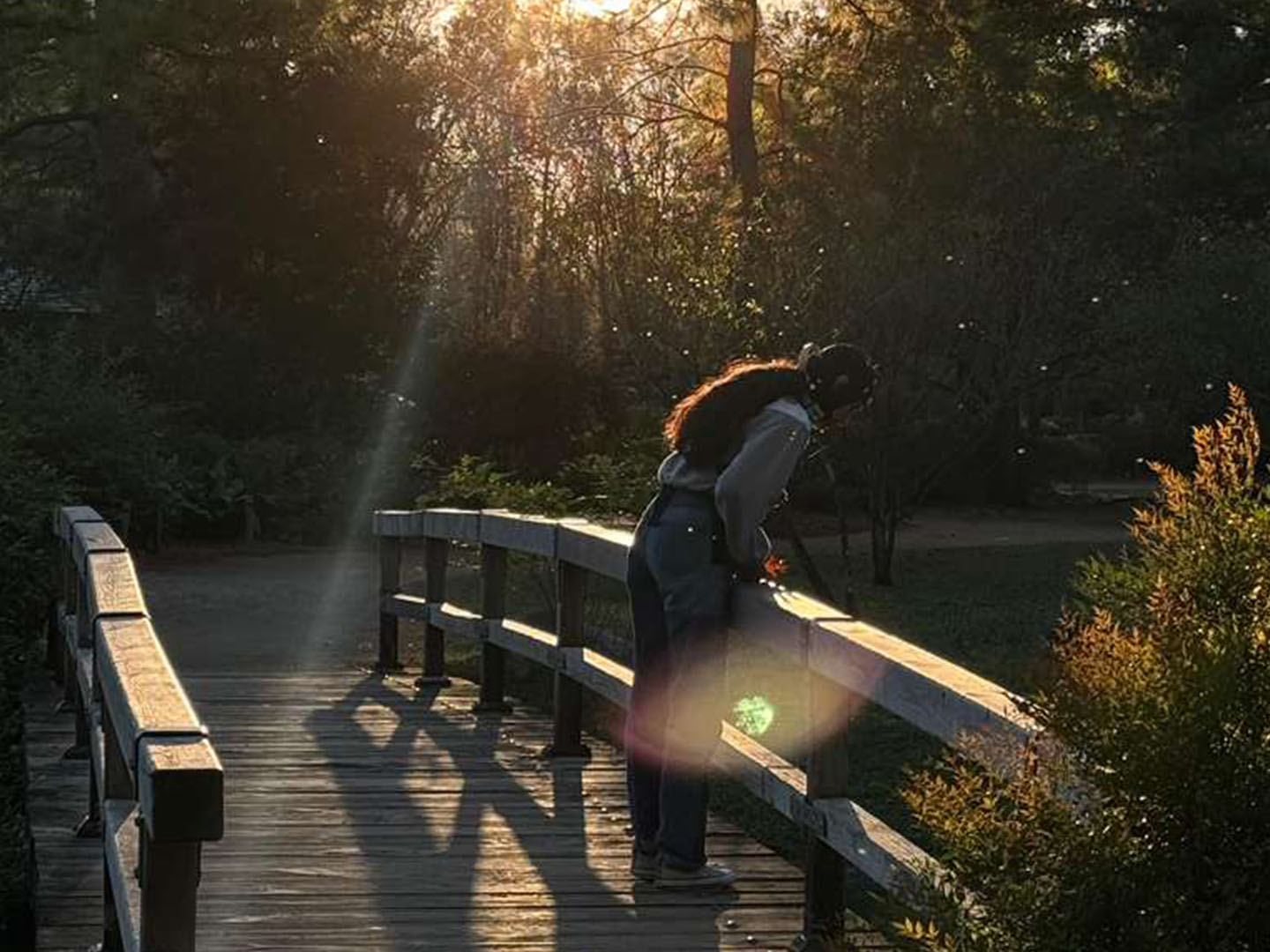 Person wearing brain cap peers over a bridge in natural park.