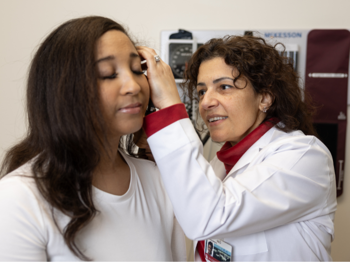 Person in white coat examining a woman's ear with an otoscope in a medical office.