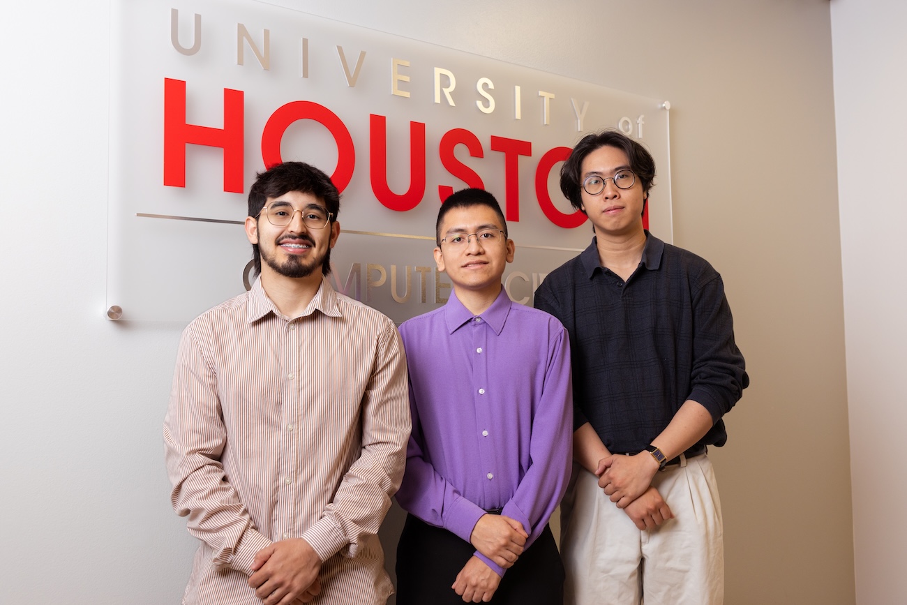 Three students stand smiling in front of a University of Houston computer science sign.