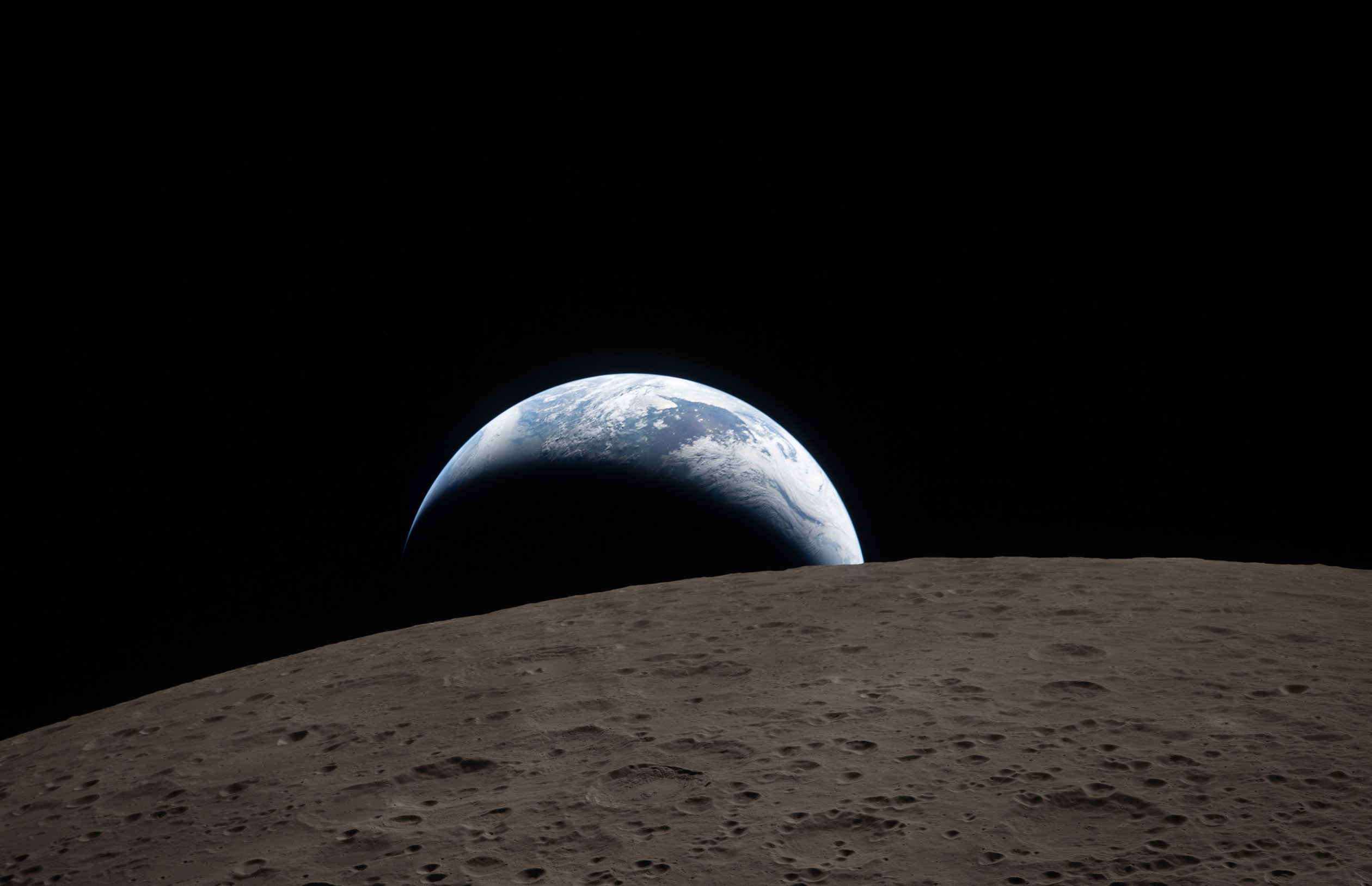 Earth rises over the cratered lunar horizon, showing a thin crescent with clouds and oceans against black space.