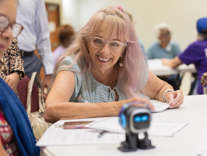 an older adult smiles at a companion robot sitting on a table