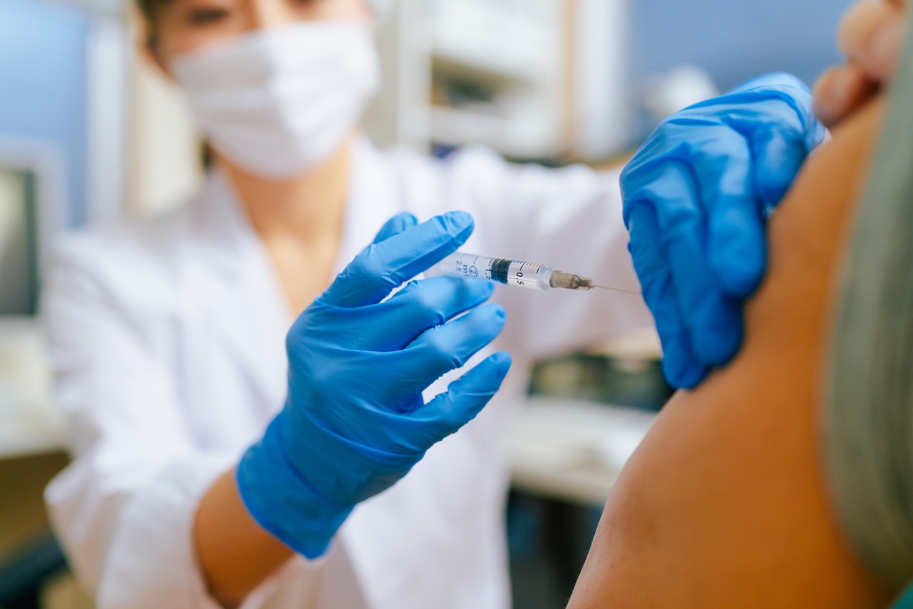 Healthcare worker in gloves administers a vaccine injection into a patient’s upper arm in a clinical setting.