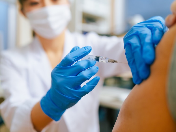 Healthcare worker in gloves administers a vaccine injection into a patient’s upper arm in a clinical setting.