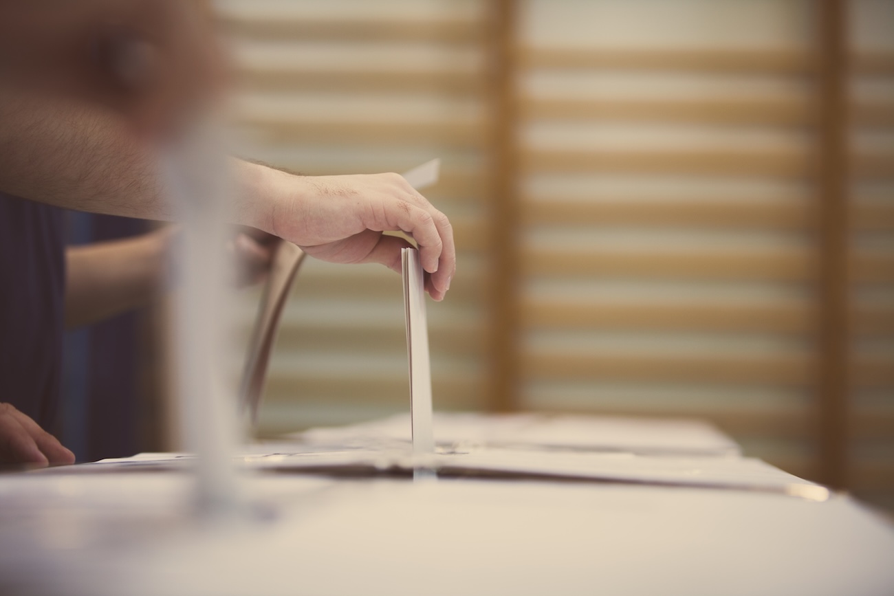 Hands place ballots into a row of ballot boxes during an election.